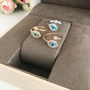 May include: Three adjustable rings with an evil eye design. The rings are made of gold, rose gold, and silver. Each ring has a blue evil eye with a white pupil and is surrounded by clear rhinestones.