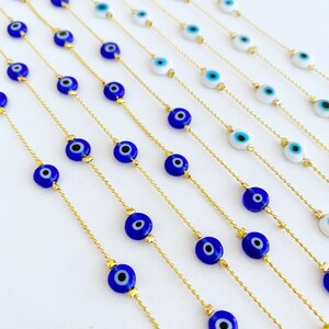 May include: Multiple gold chains with blue evil eye beads. The chains are arranged in a fan shape on a white background.