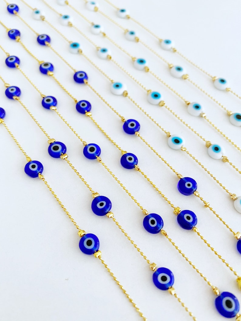 May include: Multiple gold chains with blue evil eye beads. The chains are arranged in a fan shape on a white background.