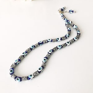 May include: A silver chain necklace with blue and white evil eye beads. The beads are oval shaped and have a silver trim.