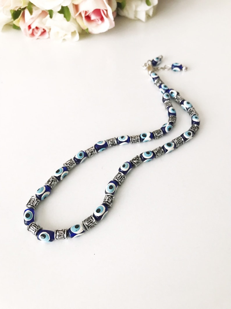 May include: A silver chain necklace with blue and white evil eye beads. The beads are oval shaped and have a silver trim.