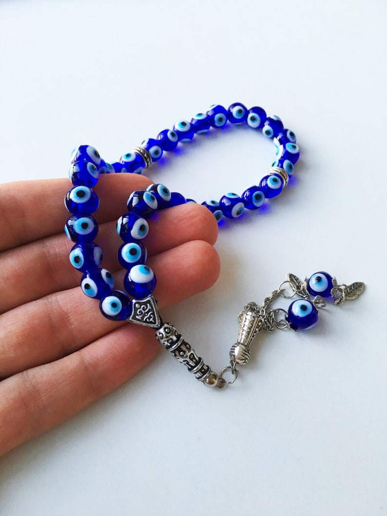Puede incluir: Un collar de cuentas de oraci&oacute;n de ojo turco azul y blanco con un dije de plata y borla. Las cuentas est&aacute;n enhebradas en una cadena de plata.