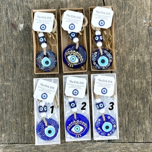 May include: Three blue and white evil eye charms with a string of beads and a small tag that reads "The Evil Eye Stare back at the world to shield you from negativity and harm".