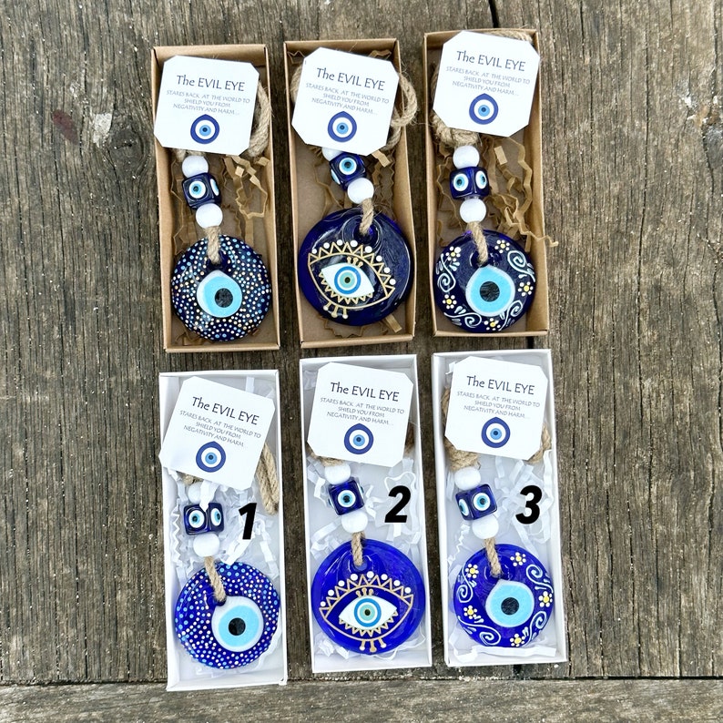 May include: Three blue and white evil eye charms with a string of beads and a small tag that reads "The Evil Eye Stare back at the world to shield you from negativity and harm".