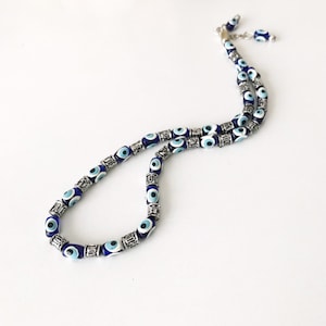 May include: A blue and silver evil eye necklace with a silver chain. The necklace is made of small beads with blue evil eyes and silver accents.