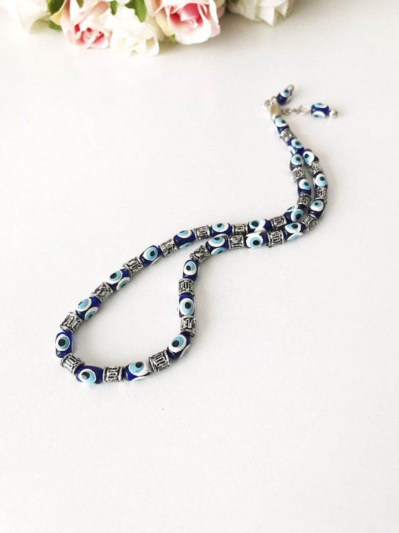 May include: A blue and silver evil eye necklace with a silver chain. The necklace is made of small beads with blue evil eyes and silver accents.