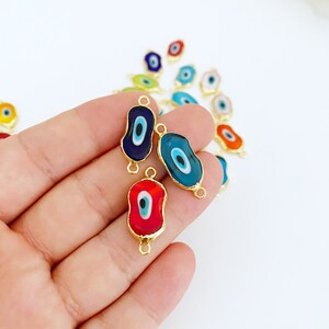 May include: Assortment of colorful evil eye charms with gold accents. The charms are shaped like an oval and have a blue, red, and turquoise evil eye design.