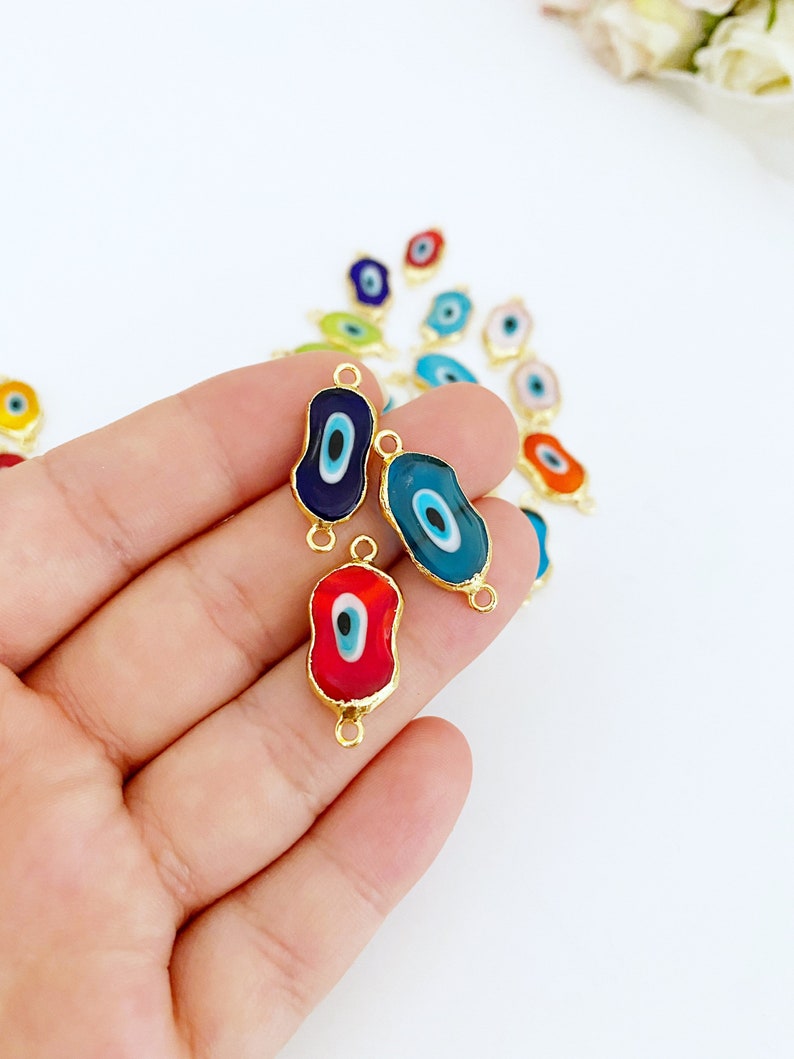 May include: Assortment of colorful evil eye charms with gold accents. The charms are shaped like an oval and have a blue, red, and turquoise evil eye design.