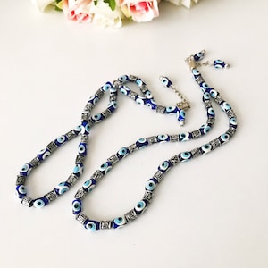May include: A blue and silver evil eye bead necklace with a silver clasp. The necklace is made of small, round beads with a blue evil eye design. The beads are separated by silver beads.