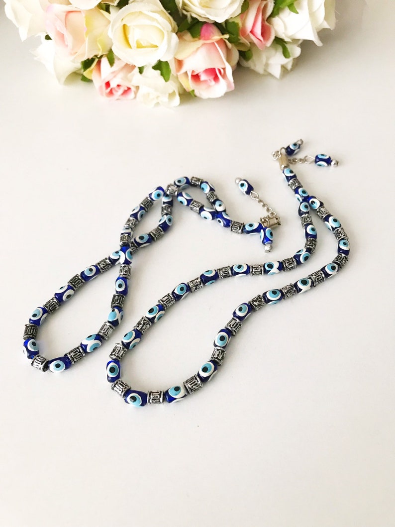 May include: A blue and silver evil eye bead necklace with a silver clasp. The necklace is made of small, round beads with a blue evil eye design. The beads are separated by silver beads.