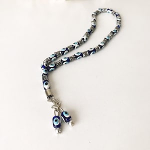May include: A blue and white evil eye bead prayer beads necklace with silver accents. The necklace has two evil eye bead charms at the end.