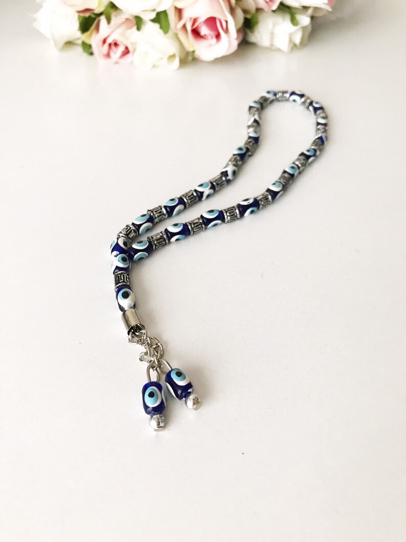 May include: A blue and white evil eye bead prayer beads necklace with silver accents. The necklace has two evil eye bead charms at the end.