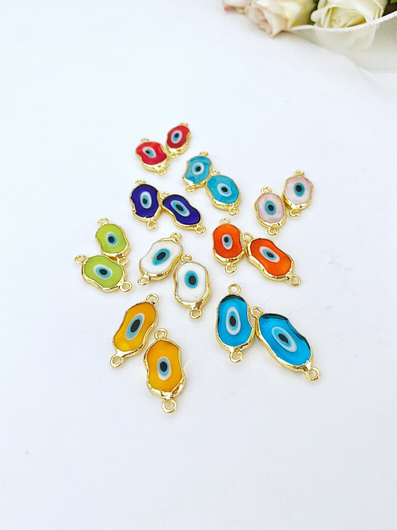 May include: Assortment of colorful evil eye charms with gold accents. Each charm features a blue eye with a white pupil and is attached to a gold jump ring.
