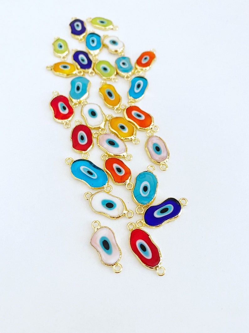 May include: Assortment of colorful evil eye charms with gold accents. The charms are oval shaped with a blue eye in the center.