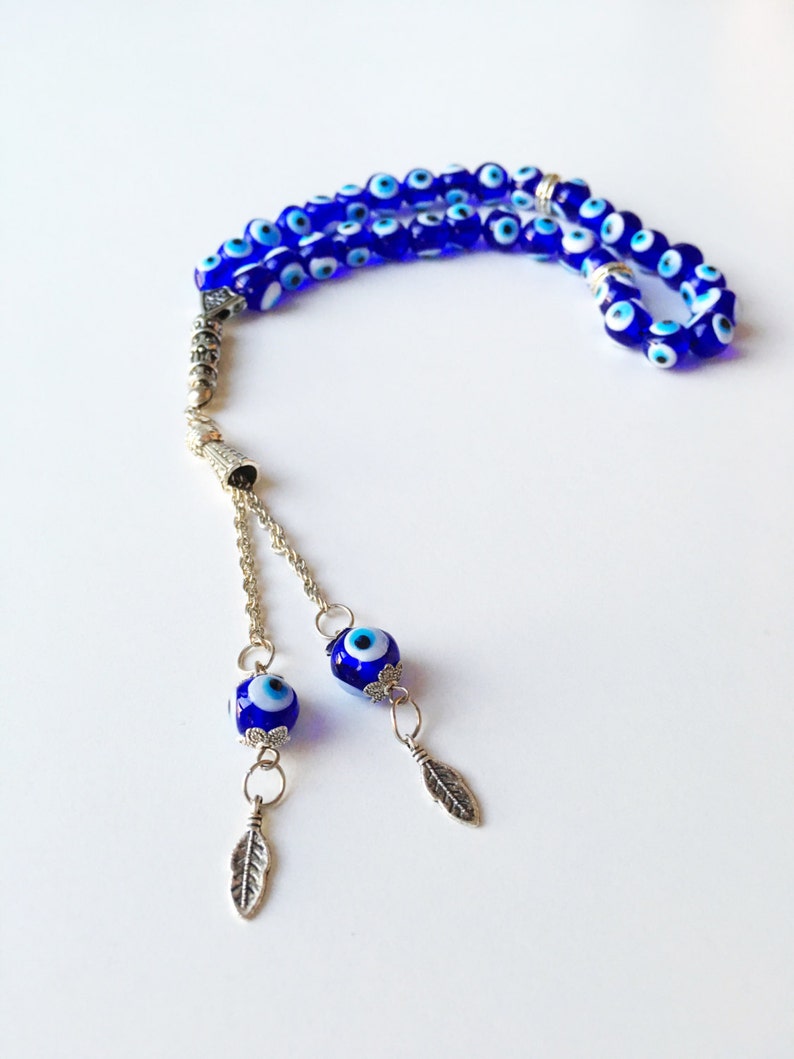 Puede incluir: Un mala de oraci&oacute;n de cuentas azules y blancas con detalles plateados y dos cuentas de ojo turco colgantes con dijes de hoja plateada.