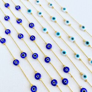 May include: Multiple gold chains with blue and white evil eye beads. The chains are laid out in rows on a white surface.