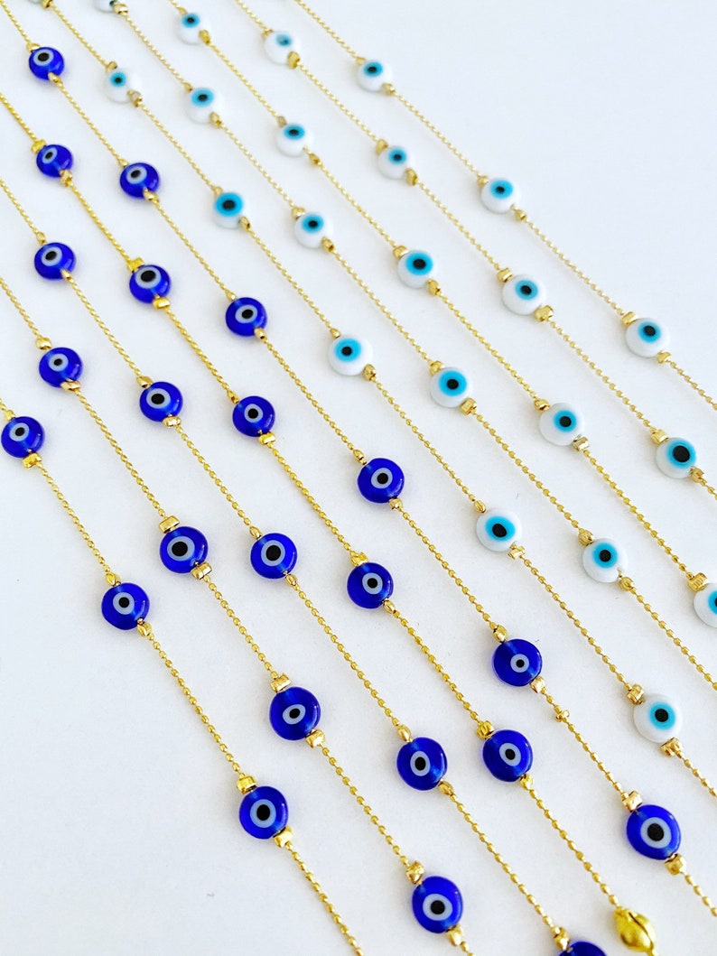 May include: Multiple gold chains with blue and white evil eye beads. The chains are laid out in rows on a white surface.