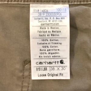 Puede incluir: Primer plano de una etiqueta Carhartt sobre tela color beige. La etiqueta incluye el logotipo de la marca, informaci&oacute;n del producto y el texto "B151 LBR 38 x 30 Loose Original Fit".