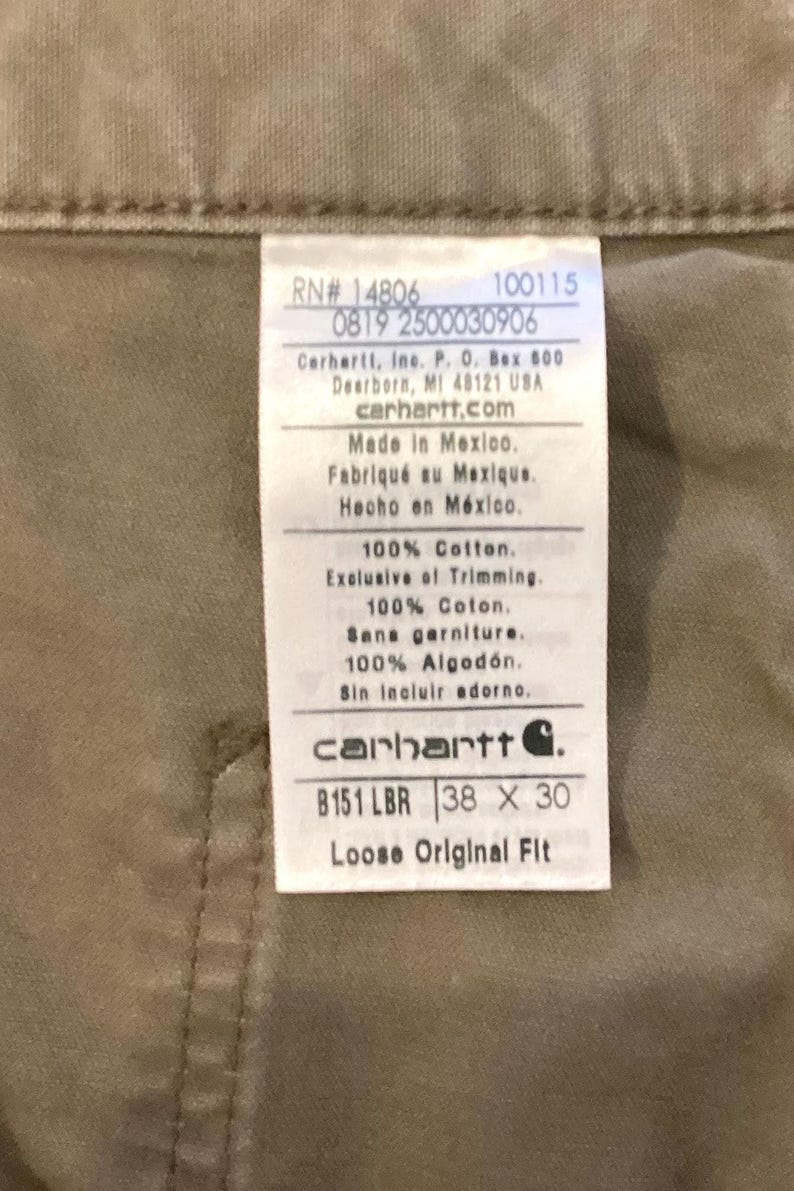 Puede incluir: Primer plano de una etiqueta Carhartt sobre tela color beige. La etiqueta incluye el logotipo de la marca, informaci&oacute;n del producto y el texto "B151 LBR 38 x 30 Loose Original Fit".