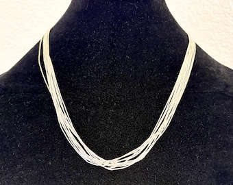 May include: A multi-strand necklace consisting of ten thin, silver-toned metallic chains that drape in a U-shape. The individual strands are uniform in color and texture, creating a layered effect that hangs evenly around the neck area.