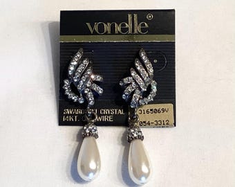 May include: A pair of Vonelle earrings on a black card. The earrings feature a silver-tone, leaf-like design encrusted with sparkling crystals. Each earring has a pear-shaped, faux pearl drop. The card reads "SWAROVSKI CRYSTAL 14KT. GOLD WIRE."