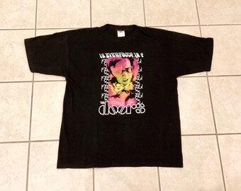 May include: Black t-shirt featuring a colorful graphic of a person with glasses and the band name "The Doors". The text "IS EVERYBODY IN?" is above the image. The band's logo is in white.