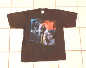 May include: A dark brown short-sleeve t-shirt featuring a graphic print of Jim Morrison and The Doors. The design includes multiple photographic images of the musician, the text "Jim Morrison" and "The Doors," and the years "1943-1971" in blue.
