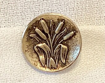 May include: A silver-toned metal button with a raised design of a bouquet of stylized flowers. The button has a smooth, slightly textured surface.