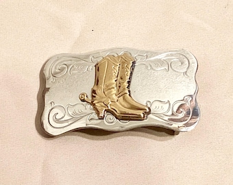 May include: Silver belt buckle with a gold-toned design of two cowboy boots with spurs.