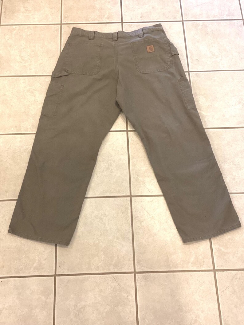 Puede incluir: Pantalones de trabajo verde oliva con m&uacute;ltiples bolsillos, incluyendo dos bolsillos traseros y dos bolsillos laterales. Los pantalones tienen un parche cuadrado marr&oacute;n con el logo en el bolsillo trasero. Los pantalones est&aacute;n hechos de un material duradero.