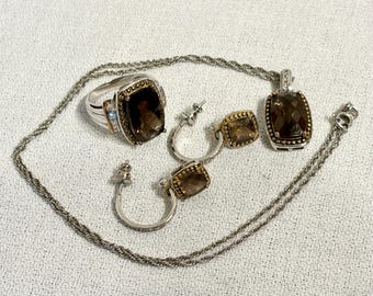 May include: A jewelry set featuring a ring, earrings, and a pendant necklace. The ring and pendant have large, square, smoky-brown gemstones set in silver and gold-toned metal. The earrings are hoop style with matching gemstones.