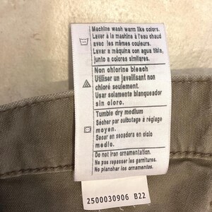 Puede incluir: Primer plano de una etiqueta de ropa con instrucciones de cuidado en varios idiomas. La etiqueta incluye instrucciones de lavado, blanqueo y secado. La etiqueta tambi&eacute;n tiene el n&uacute;mero "2500030906 B22" impreso.