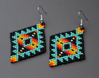 May include: A pair of beaded earrings with a geometric design. The earrings are black with turquoise, orange, yellow, and white accents. The earrings have a diamond shape and silver hooks.