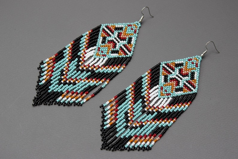 Pode incluir: Um par de brincos de contas com um design geom&eacute;trico. Os brincos apresentam uma parte superior quadrada com um padr&atilde;o de contas turquesa, pretas, brancas, vermelhas e laranja. Longas franjas pendem da parte inferior, com contas pretas, turquesas e brancas.