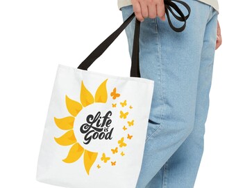 Peut inclure: Sac fourre-tout blanc avec un tournesol jaune et du texte noir qui dit "Life is Good". Le tournesol est entouré d'un cercle de papillons jaunes.