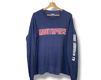 May include: Navy blue long-sleeve shirt with the word "MOUTHPIECE" in red and white block letters across the chest. The right sleeve has the text "NJ STRAIGHT EDGE" in white. The shirt is hanging on a wooden hanger.