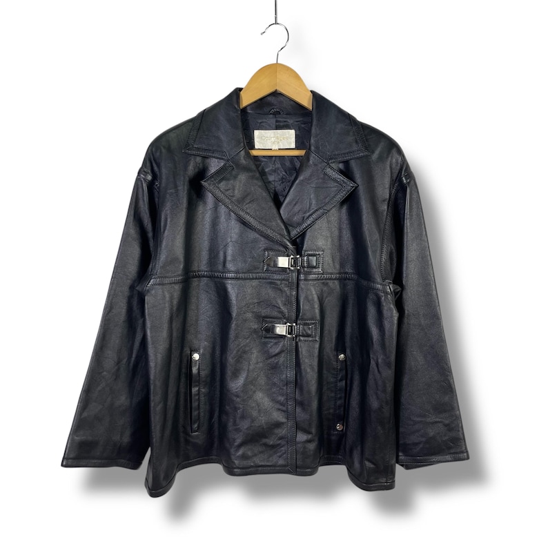 May include: A black leather jacket with a silver buckle closure and a collar. The jacket has a slightly oversized fit and a relaxed silhouette.