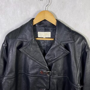 May include: Black leather jacket with a buckle closure and a collar. The jacket has a  stitched design and a label that reads "Genuine Leather".