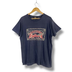 May include: A navy blue short-sleeve t-shirt featuring a graphic print of a red truck with the text Ralph Lauren Double RL and Seasons Greetings. The design is framed by a decorative border with holly accents on a crew neck cotton garment.