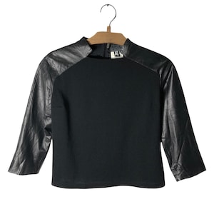 May include: Black top with long sleeves made of leather. The sleeves are black leather and the body of the top is black knit.