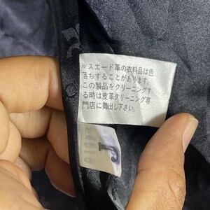 May include: A black tag with white text that reads: "Suede leather garments are prone to color fading. When cleaning this product, use a leather cleaning specialist."