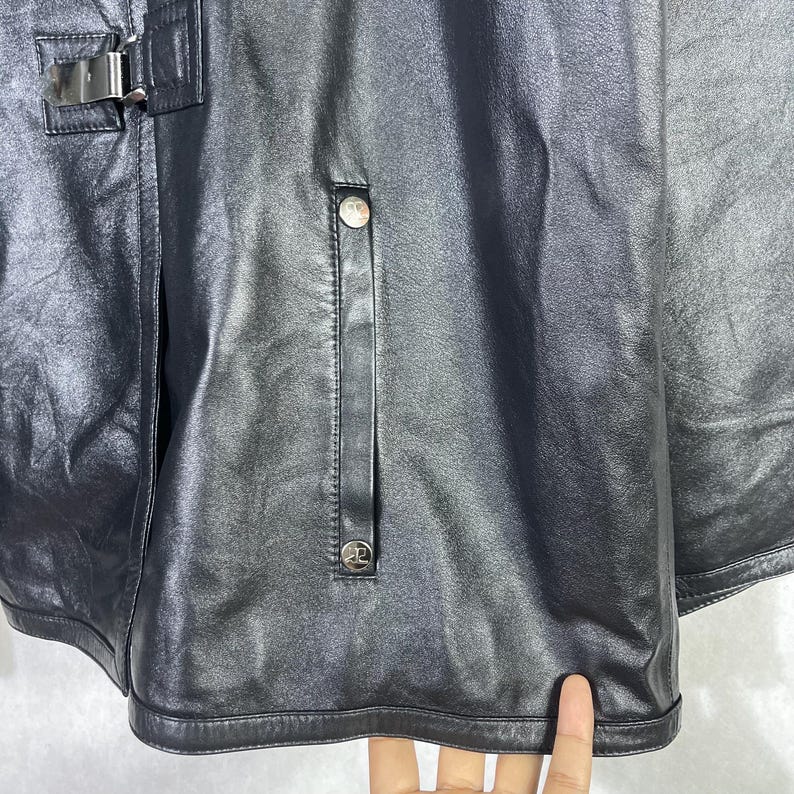 May include: Black leather jacket with a zipper closure and a snap button detail. The jacket has a long sleeve design and a collar.