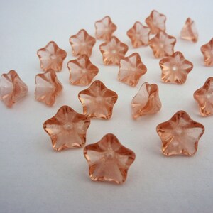 May include: A collection of peach-coloured glass star-shaped beads with a raised centre. The beads have a slightly frosted finish.