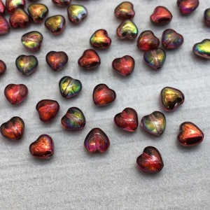 Peut inclure: Un ensemble de perles en verre en forme de cœur irisées dans des tons de rouge, orange et or. Les perles ont une finition chatoyante et réfléchissante.