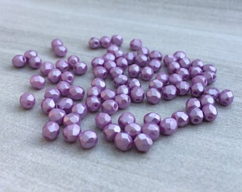 May include: A group of small, faceted, purple glass beads. The beads have a shiny, iridescent finish.