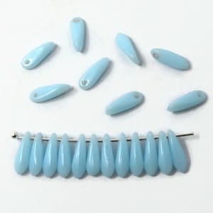 May include: A strand of light blue glass beads in a teardrop shape. The beads are strung on a silver wire and are arranged in a row. There are also several loose beads scattered around the strand.