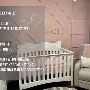 May include: Gold-colored vinyl wall decal with the names "Ella" and "Grace" in a cursive font. The decal is displayed on a pink wall with a geometric pattern. The decal is 42 inches wide. The text "FINISH: GOLD" and "SIZE: 42" W (ELLA IS 42" W)" is visible in the image.
