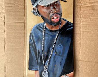 May include: A hand-painted skateboard deck featuring a portrait of a man wearing a black t-shirt, a gray mesh baseball cap, and a silver chain with a pendant. The man has a beard and is looking to the right.