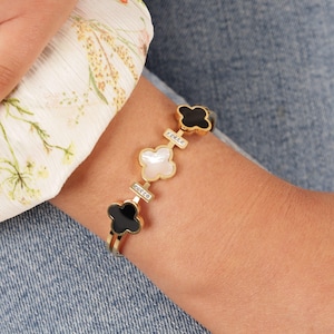 May include: Gold bracelet featuring a series of black and white clover charms. Each charm is embellished with small clear rhinestones.
