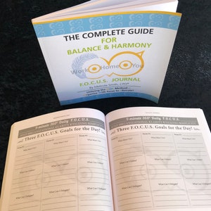 May include: An open book with a blue and yellow owl design on the cover. The title of the book is "The Complete Guide for Balance & Harmony Work Home You F.O.C.U.S. Journal". The book has a section titled "9-minute 360&deg; Daily F.O.C.U.S. Find Organizational Clarity Utilizing Simplicity Three F.O.C.U.S. Goals for the Day!" with a table for listing goals.